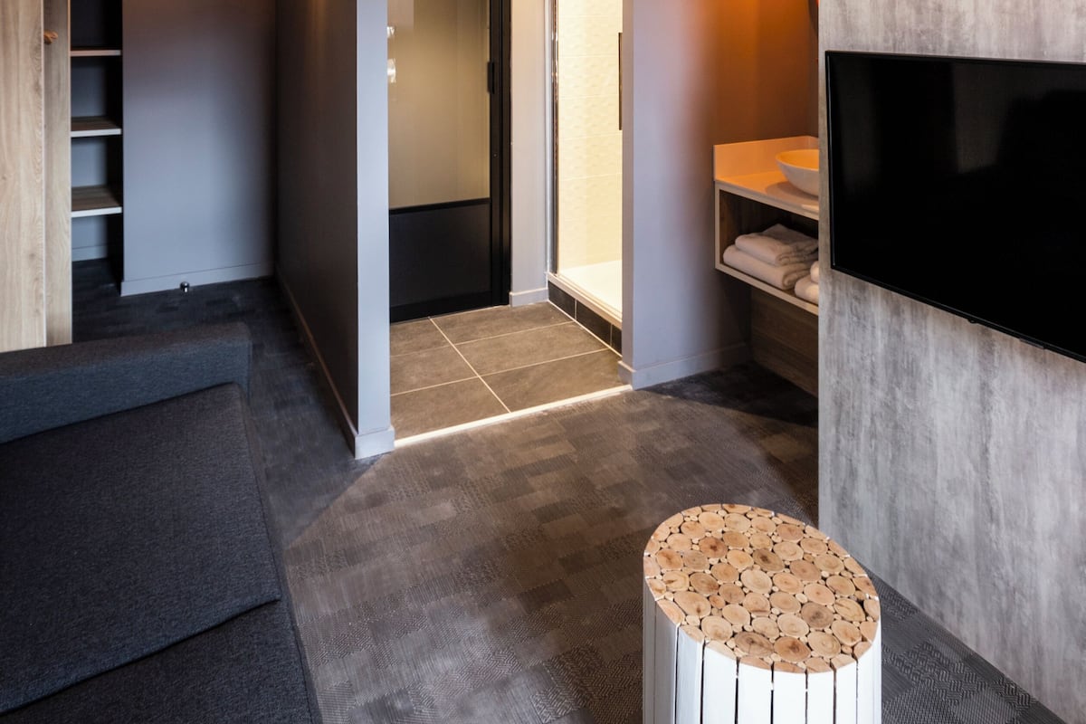 Een ruime loft met een hoge plafond, een trap met houten leuning, een grote flatscreen televisie aan de wand, en een gezellige zithoek met een rond poef.
