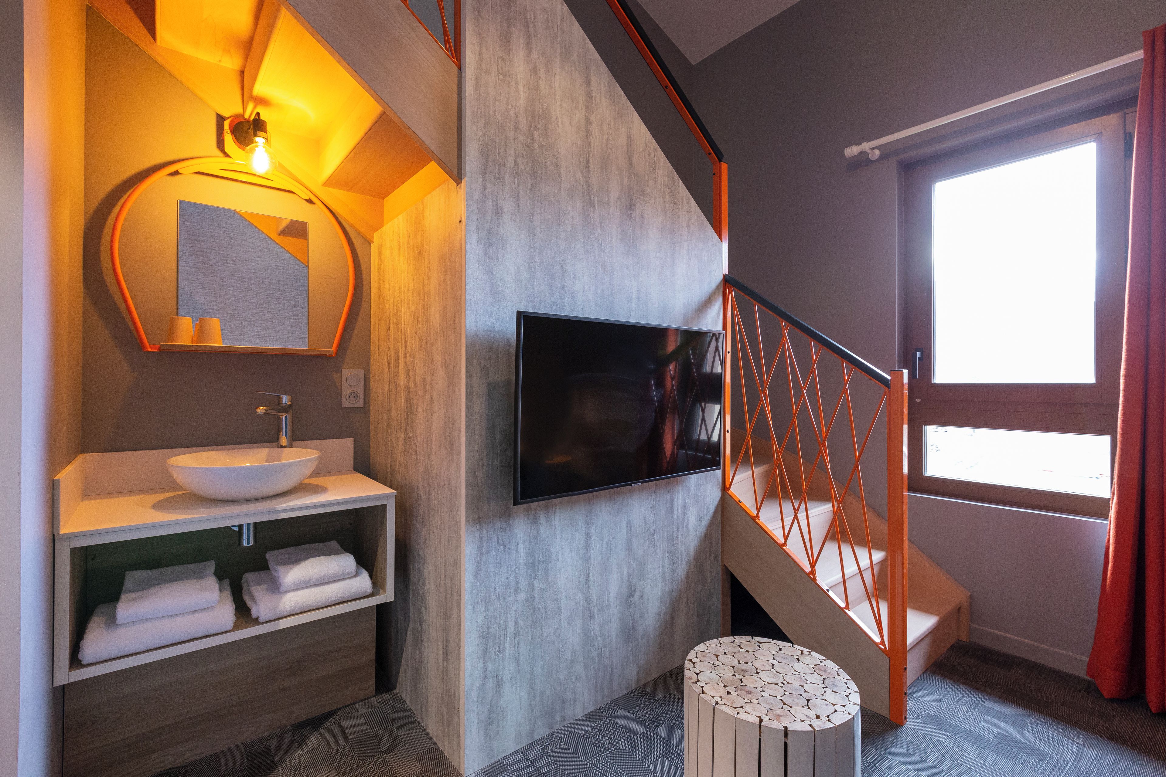Een moderne badkamer met een grote spiegel, een witte wastafel en een flatscreen televisie aan de muur.