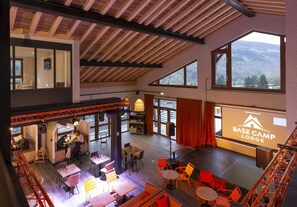 A spacious indoor area with multiple seating arrangements, a stage, and large windows offering mountain views. - Base Camp Lodge (Bourg-Saint-Maurice)