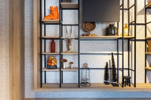 A room with a wooden floor, a black metal shelf unit, and a variety of decorative items including a vase, a small tree, and a bottle.