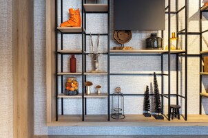 A room with a wooden floor, a black metal shelf unit, and a variety of decorative items including a vase, a small tree, and a bottle.