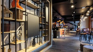 A modern interior with wooden flooring, metal shelving with books and decorative items, and a bar area with stools and a counter. - Base Camp Lodge (Bourg-Saint-Maurice)