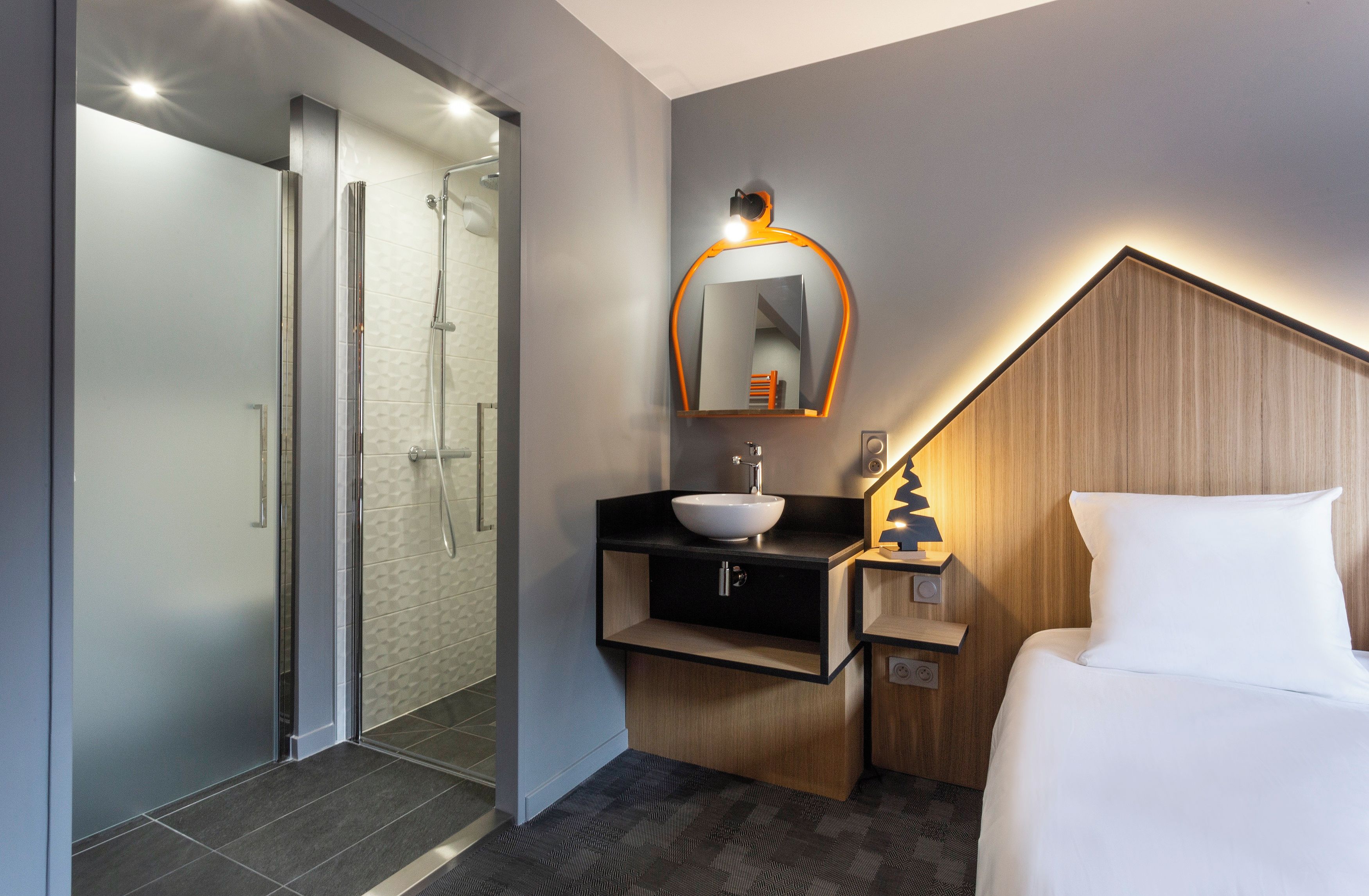 Habitación de hotel con ducha, lavabo, mesita de noche con lámpara y cama.