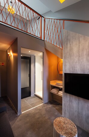A modern interior with a staircase, a flat-screen TV mounted on a wall, and a small round table. - Base Camp Lodge (Bourg-Saint-Maurice)