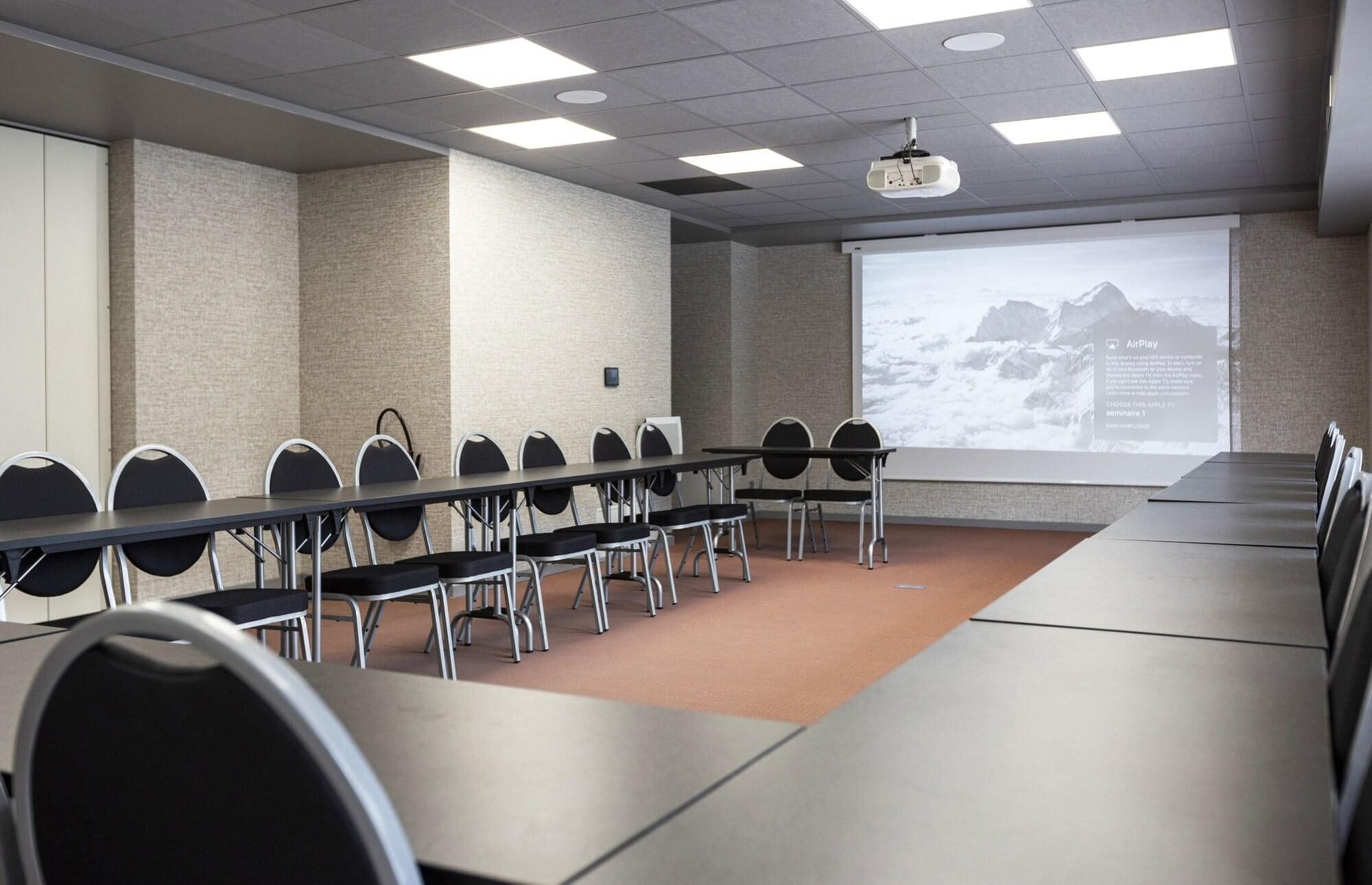 Une salle de conférence équipée d’une longue table, de chaises, d’un écran de projection et d’un grand écran affichant une présentation.