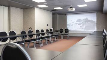 Une salle de conférence équipée d’une longue table, de chaises, d’un écran de projection et d’un grand écran affichant une présentation.