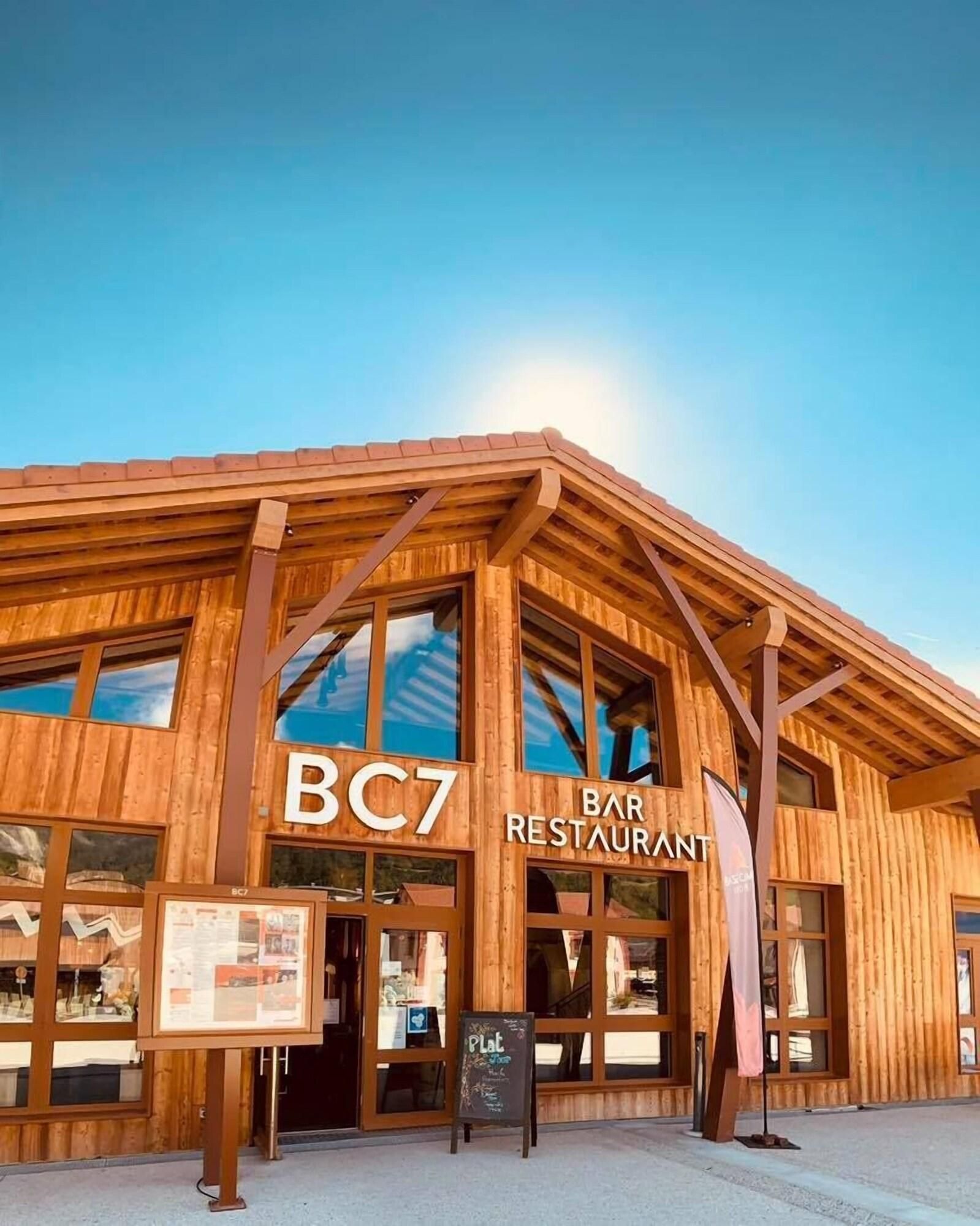 Un bâtiment en bois doté de grandes fenêtres et d’une enseigne indiquant « BC7 : BAR RESTAURANT ».
