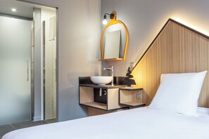 Ett modernt hotellrum med en stor säng, en sänggavel i trä, ett inbyggt handfat och en duschhörna.