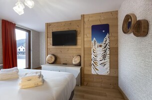 Habitación de hotel con cama, televisor montado, pintura de una montaña nevada y decoración de madera en las paredes.
