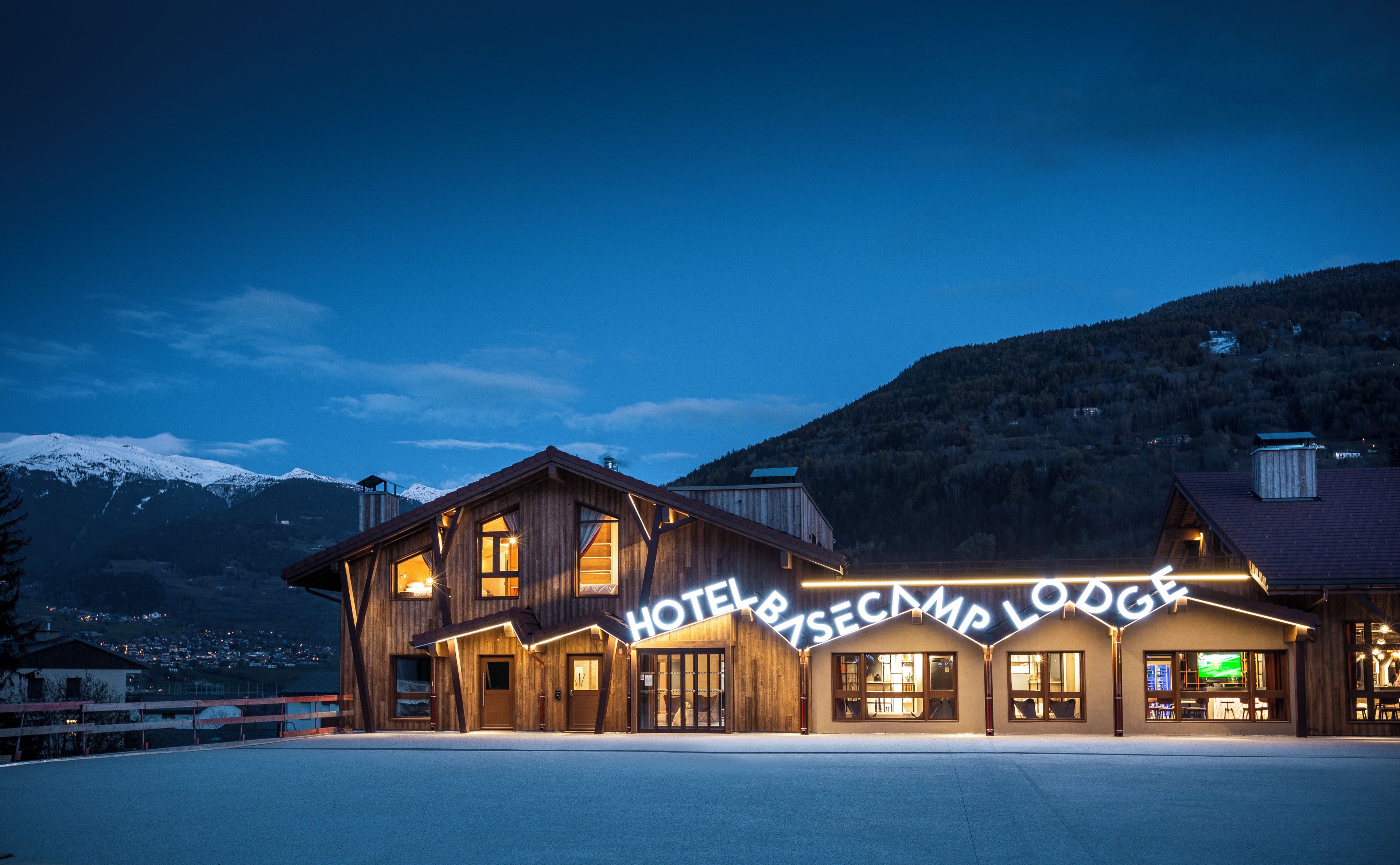 Ein hölzernes Hotel mit einem Schild, auf dem 'HOTEL & RESCUE CAMP LODGE' steht, vor einer Bergkulisse.