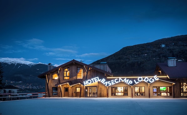 A wooden hotel with a sign reading 'HOTEL & RESCUE CAMP LODGE' against a mountainous backdrop.