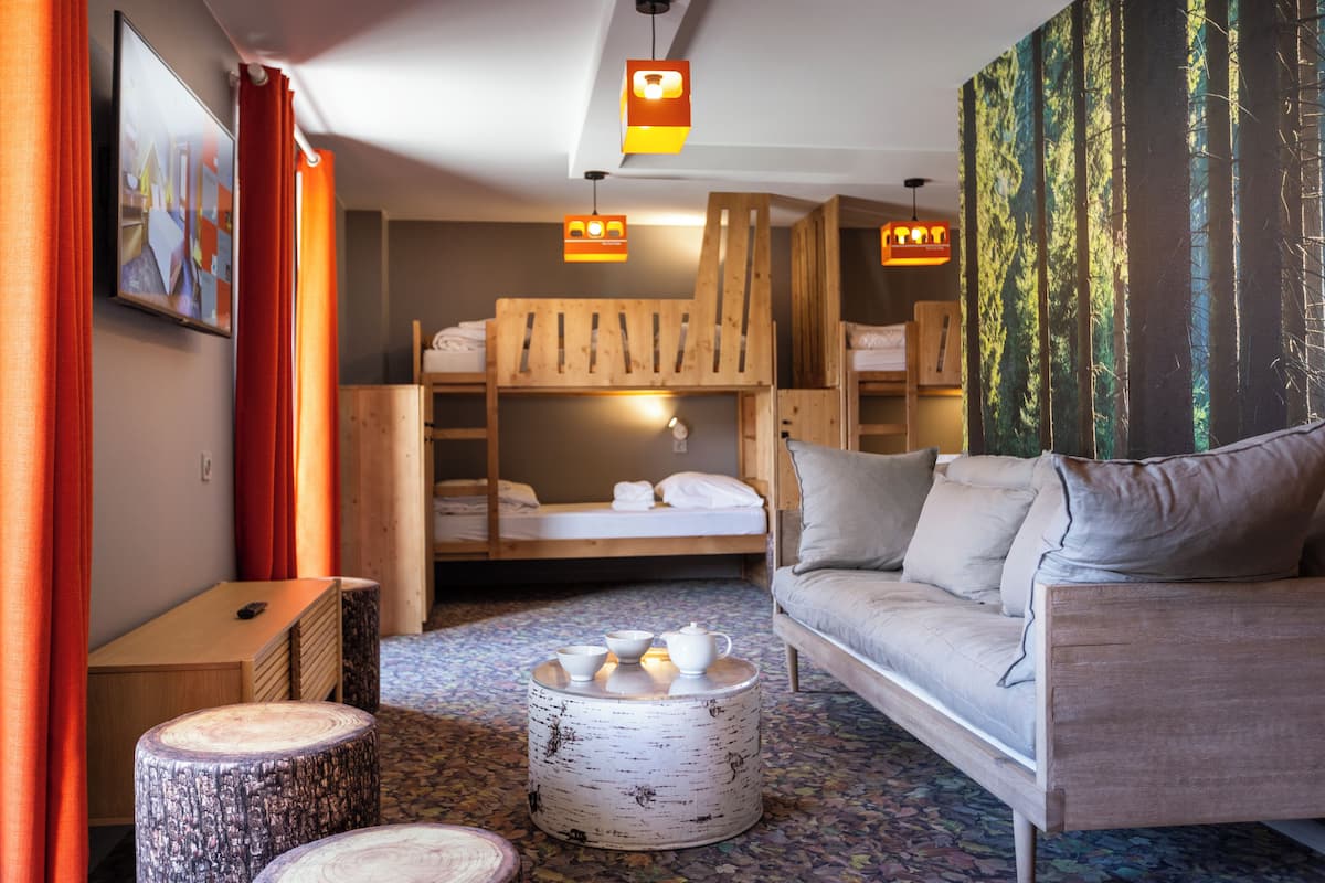 Een moderne kamer met een bank, een stapelbed, een ronde houten tafel en een schilderij van een bos.