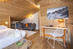 Una habitación acogedora con cama, escritorio, silla, sofá y televisor montado en la pared.
