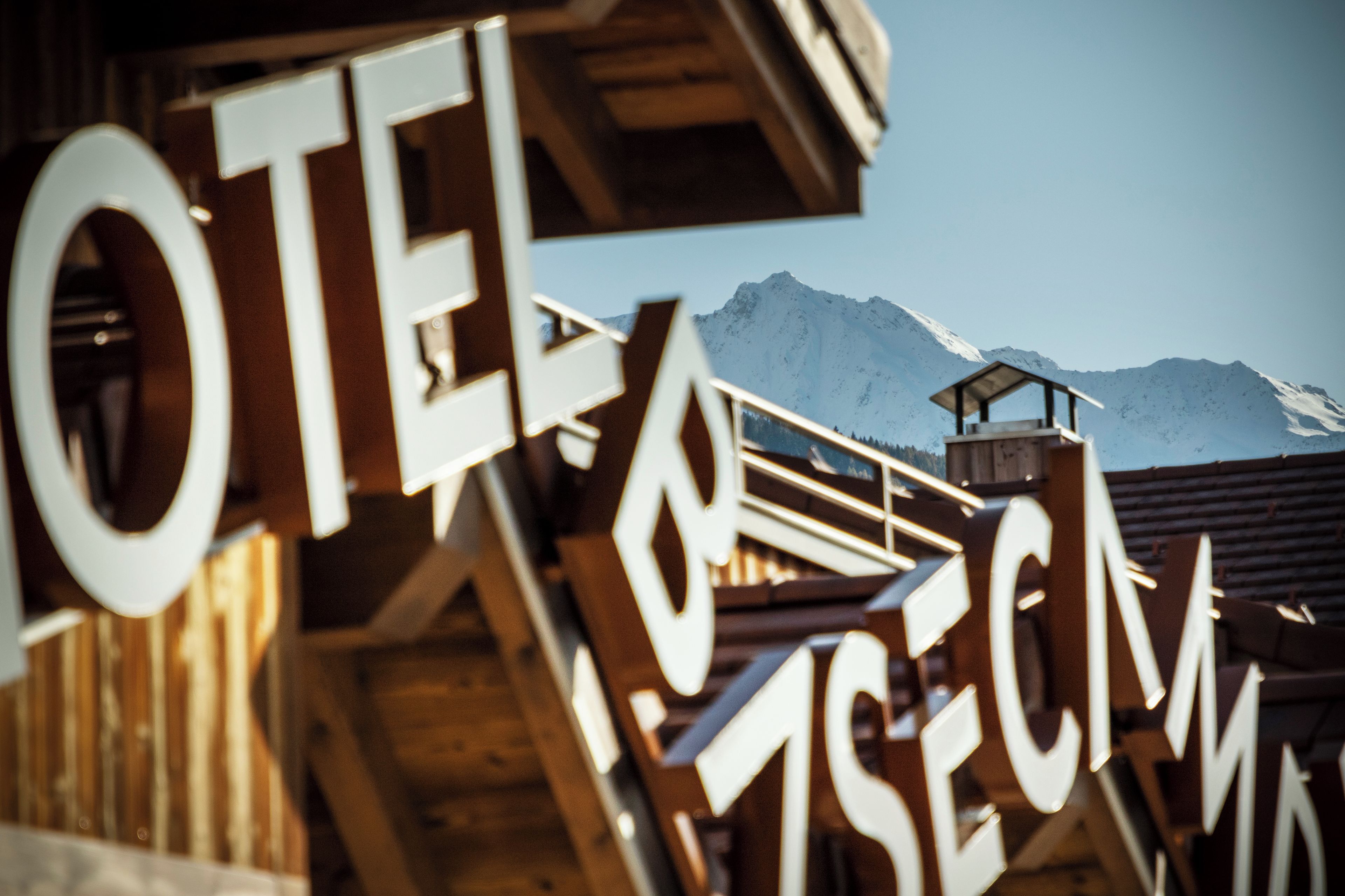 Een houten constructie met grote witte letters waarop “HOTEL” en “SECKNAGG” staan, voor een achtergrond van met sneeuw bedekte bergen.