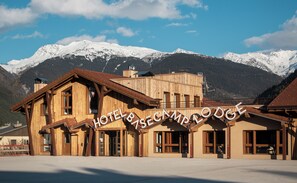 A wooden building with a sign reading "HOTEL Bise Camm Lodge" in front of snow-covered mountains. - Base Camp Lodge (Bourg-Saint-Maurice)
