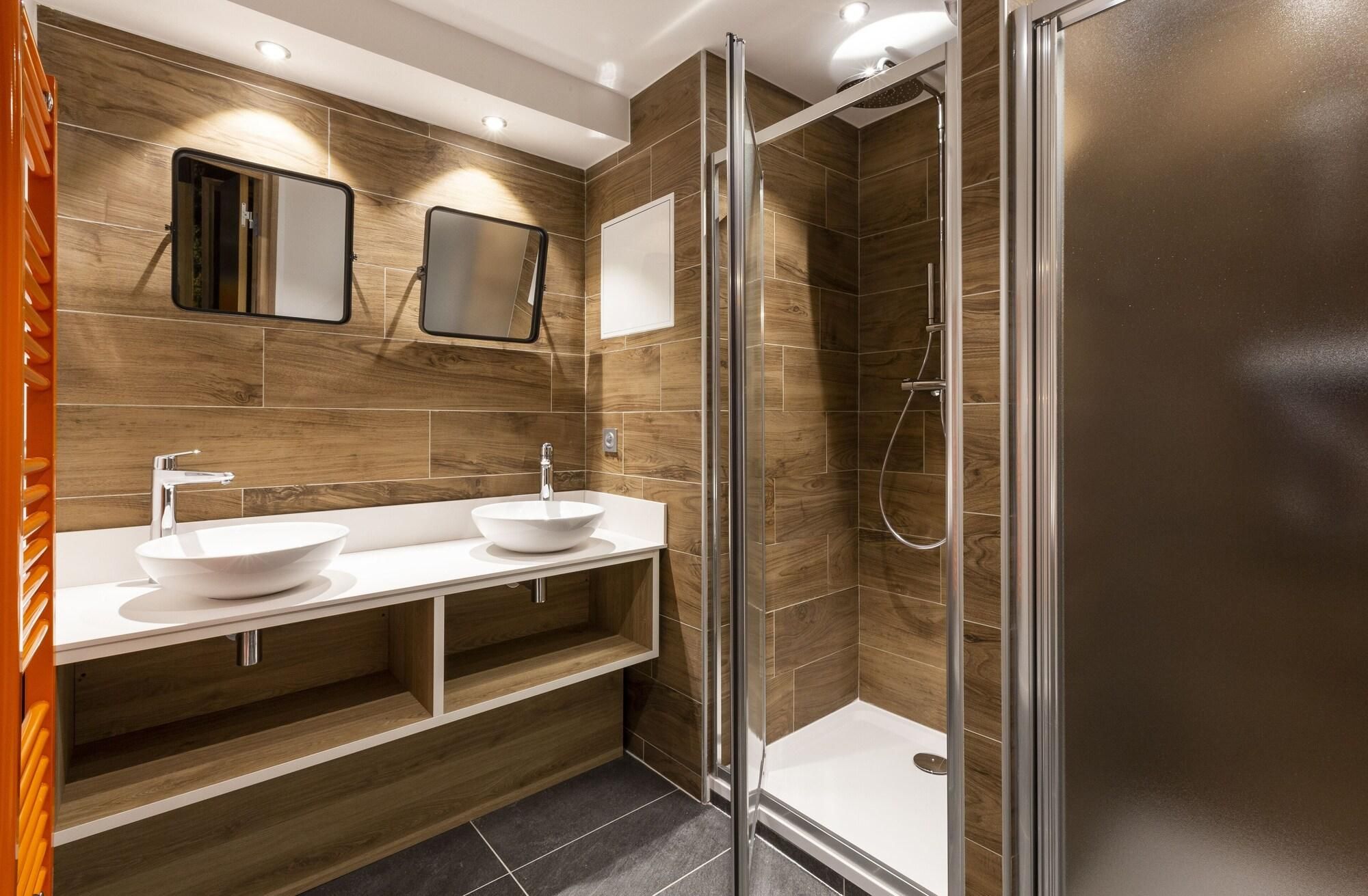 A modern bathroom with two sinks, a shower, and a mirror.