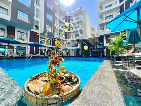 A swimming pool with lounge chairs and umbrellas, surrounded by modern buildings.
