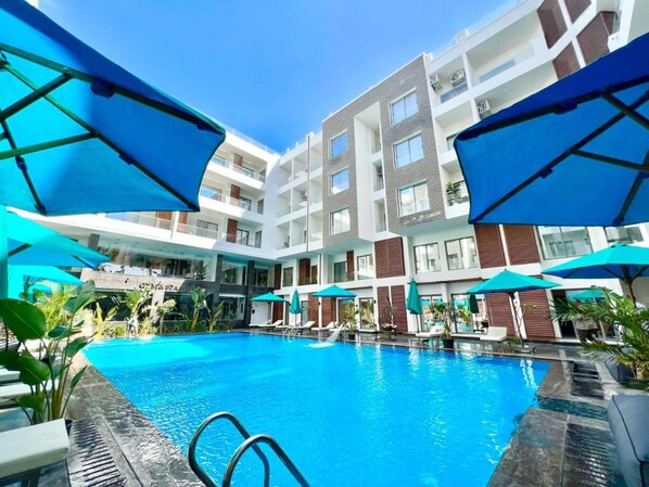 A modern hotel with a central swimming pool, multiple balconies, and outdoor umbrellas. - Hurghada - Apartment - Sleeps 6 - Pool - Parking (Hurghada)