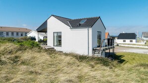 A modern white house with a sloped roof, large windows, and a small deck. - Lovely home in Thisted with kitchen (Thisted)