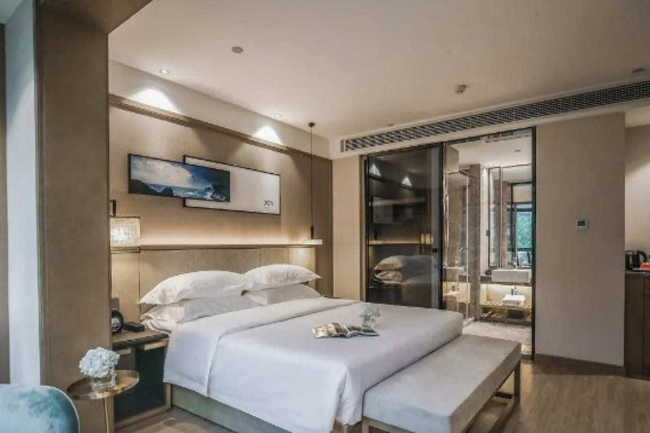 A modern hotel room with a large bed, bedside tables, a mirror, and a view of the outside.