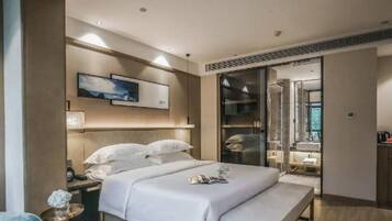 A modern hotel room with a large bed, bedside tables, a mirror, and a view of the outside.