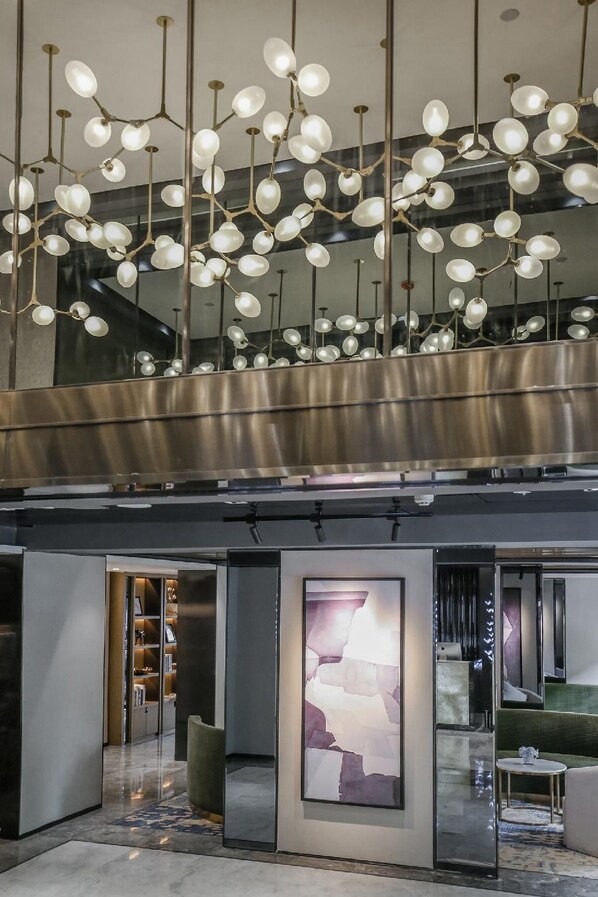 Eine moderne Lobby mit hoher Decke, einem zentralen Kunstwerk und einer Sitzecke mit einem grünen Sofa und einem kleinen runden Tisch.