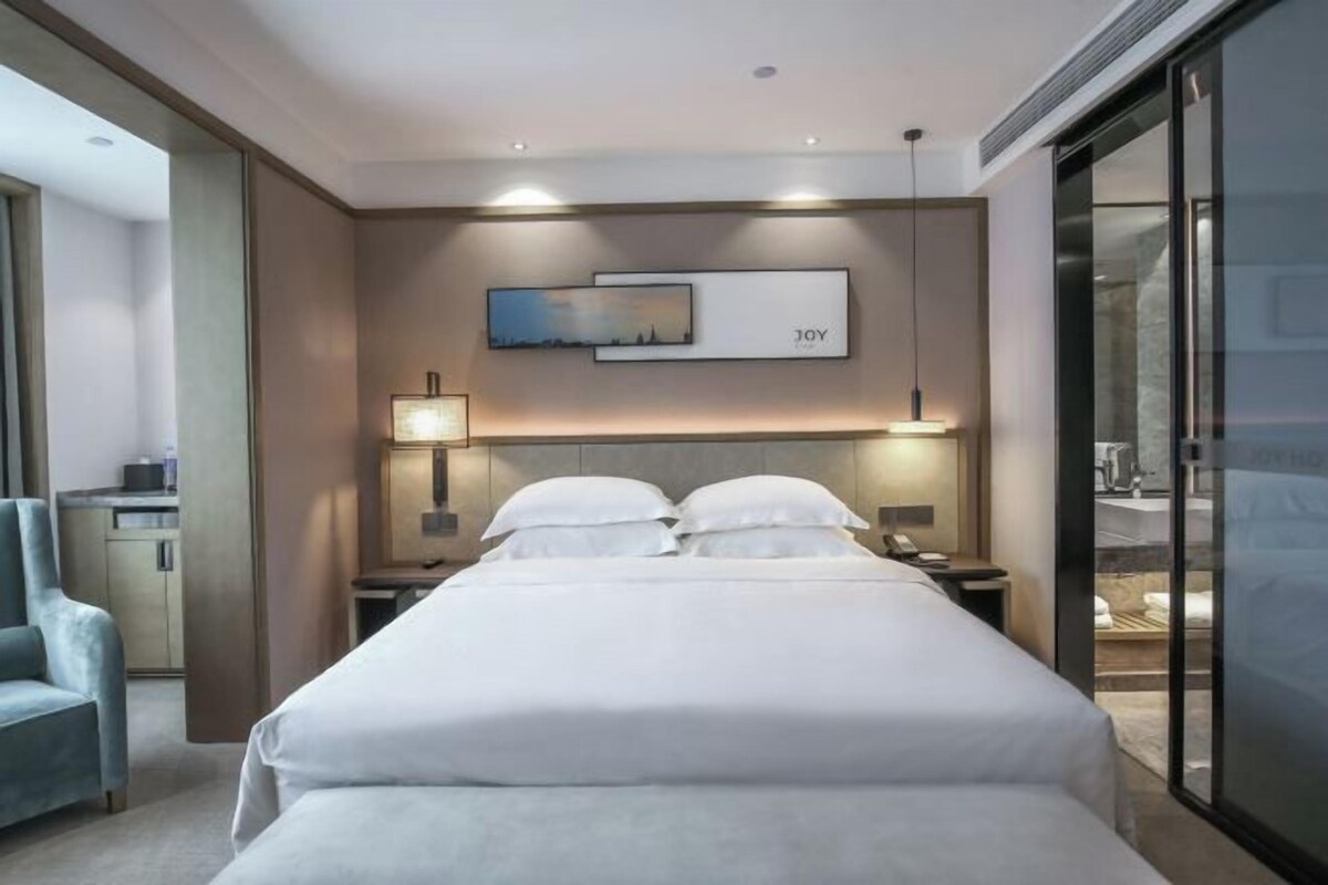 A hotel room with a bed, bedside tables, a lamp, a chair, and a painting on the wall.