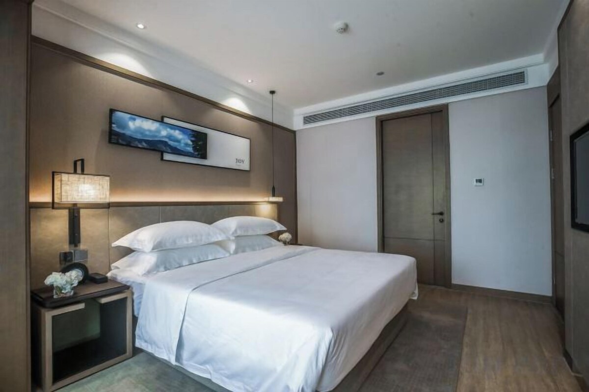 A hotel room with a bed, bedside table, lamp, and a wall-mounted TV.