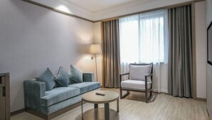 A hotel room with a sofa, armchair, round coffee table, and a TV. - Joy Hotel Hangzhou (Hangzhou)