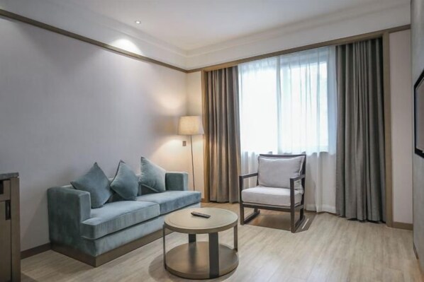 A hotel room with a sofa, armchair, round coffee table, and a TV. - Joy Hotel Hangzhou (Hangzhou)