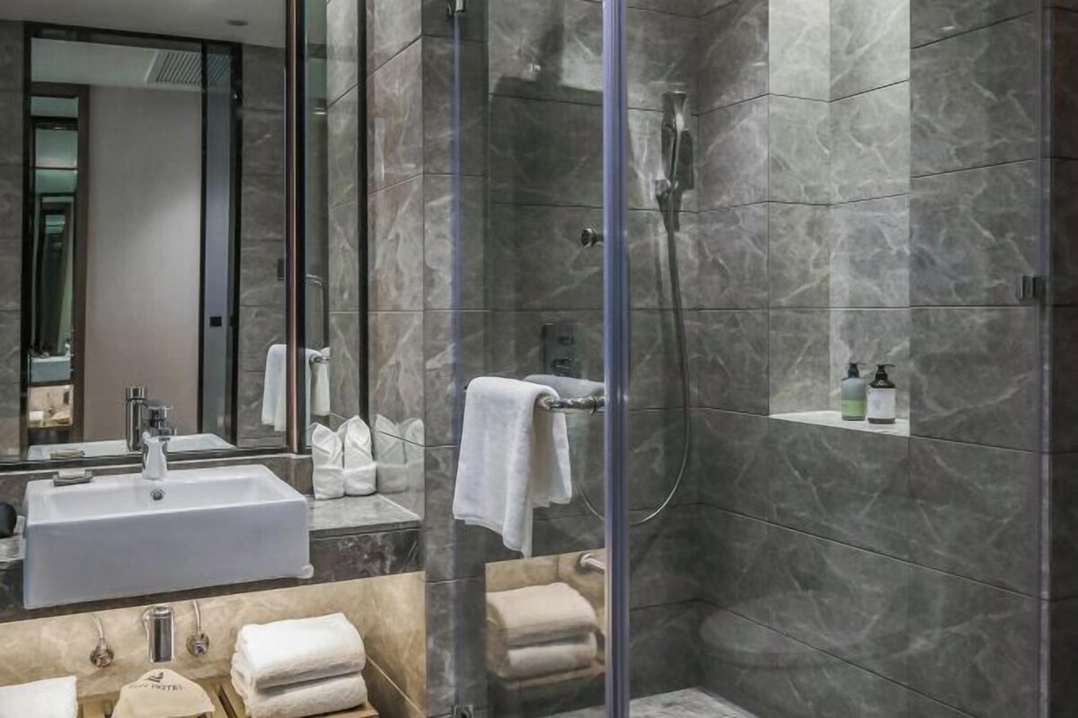 Un baño moderno con ducha de vidrio, un espejo grande, un lavamanos blanco y toallas ordenadas.