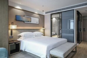 A modern hotel room with a large bed, bedside tables, a wall-mounted lamp, and a sliding glass door to a bathroom. - Joy Hotel Hangzhou (Hangzhou)