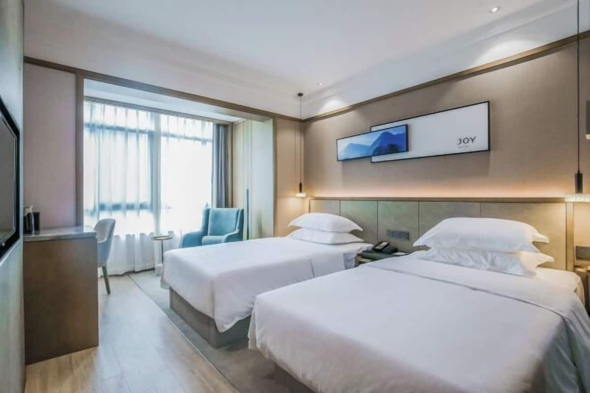 A hotel room with two beds, a desk, a chair, a TV, and a window with curtains.