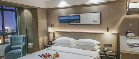 A hotel room with a bed, a nightstand, a lamp, a chair, and a window with a city view.
