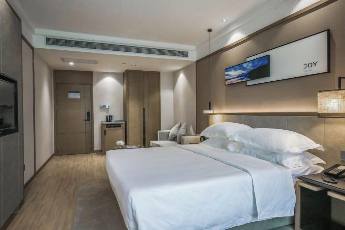 A hotel room with a bed, a TV, a desk with a lamp, and a wall-mounted artwork.
