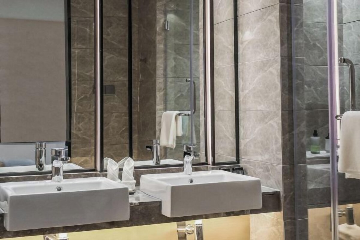 A modern bathroom with two sinks, a large mirror, and a glass shower enclosure.