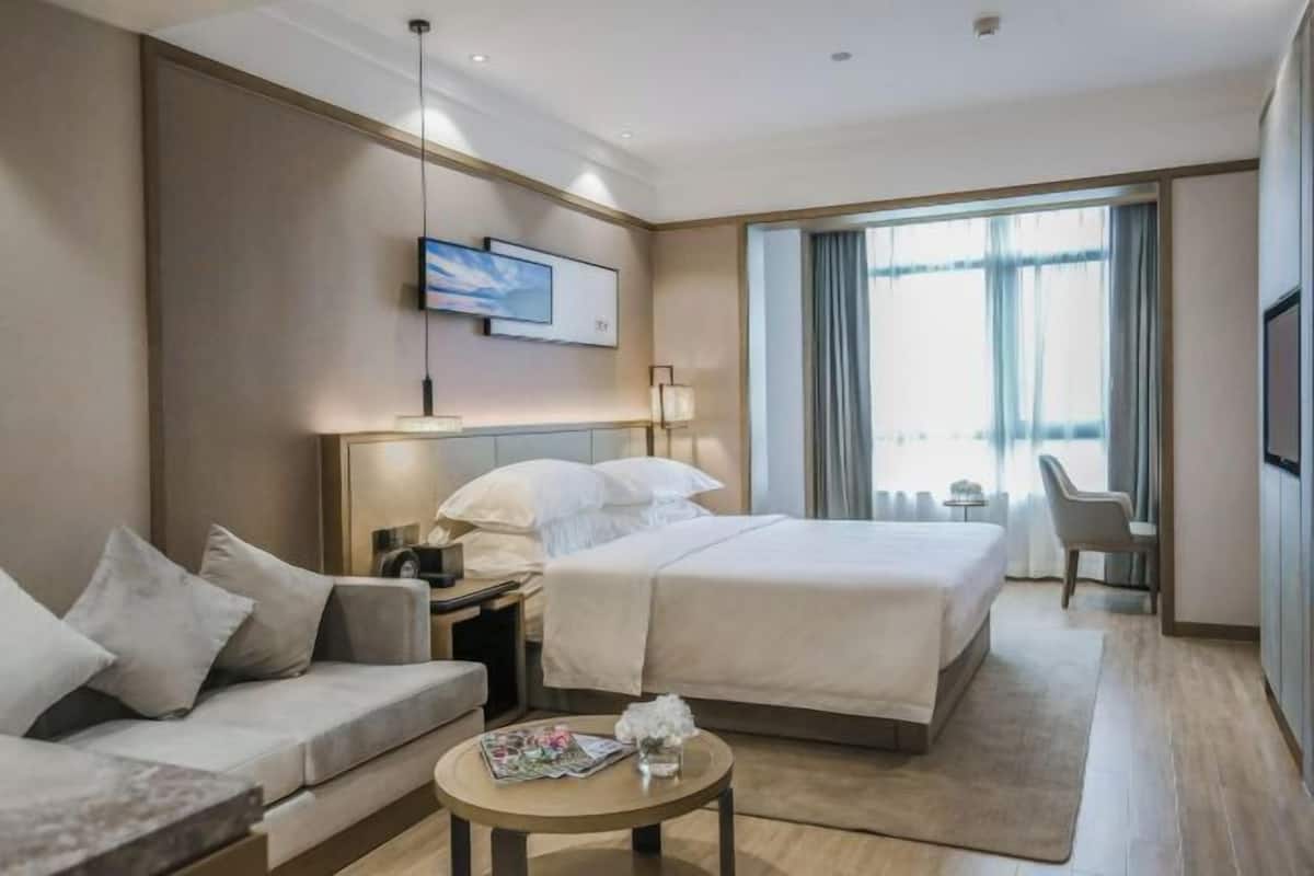 A hotel room with a bed, a sofa, a small table, a TV, and a window with curtains.