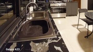 Une cuisine moderne dotée d’un plan de travail en marbre noir et blanc, d’un évier en acier inoxydable, de meubles en bois, d’une cuisinière à gaz et d’un four à micro-ondes.