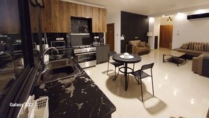 Une cuisine moderne équipée d’une cuisinière, d’un évier et de placards, un coin repas avec une table et des chaises, et un salon avec un canapé et un téléviseur.