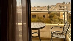 Un balcon avec une table ronde et deux chaises, offrant une vue sur un paysage urbain avec des bâtiments et un ciel partiellement nuageux.
