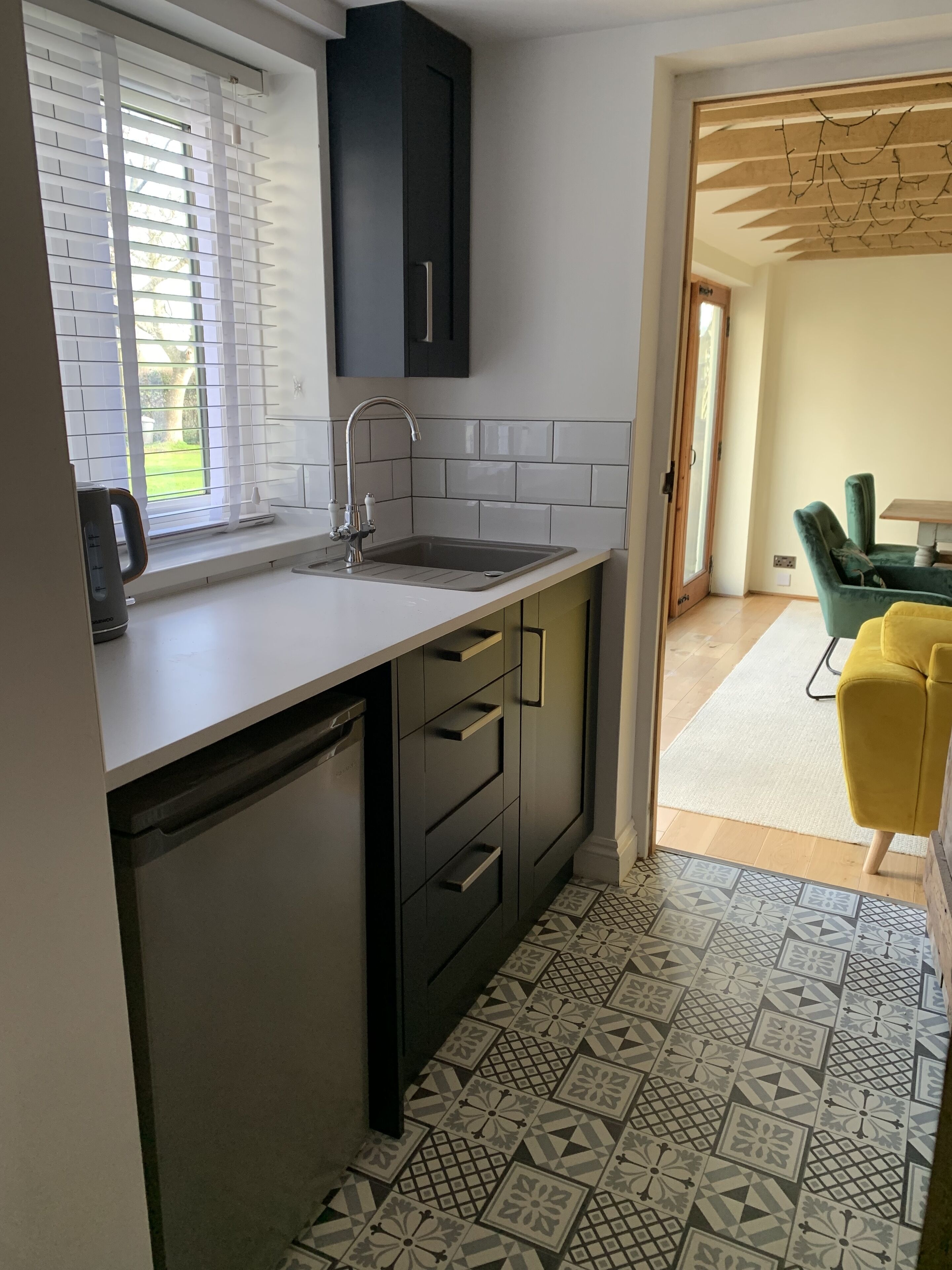 Una cocina moderna con lavavajillas integrado, un lavamanos con grifo y una ventana con persianas.