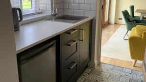 A modern kitchen with a built-in dishwasher, a sink with a faucet, and a window with blinds. - River and country views & woodburner at ‘The Nest’ (Burrowbridge)