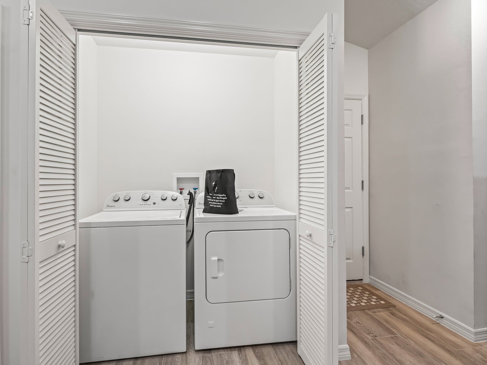 A laundry room with two white front-loading washers and dryers, a black bag on the dryer, and a white door with a handle.
