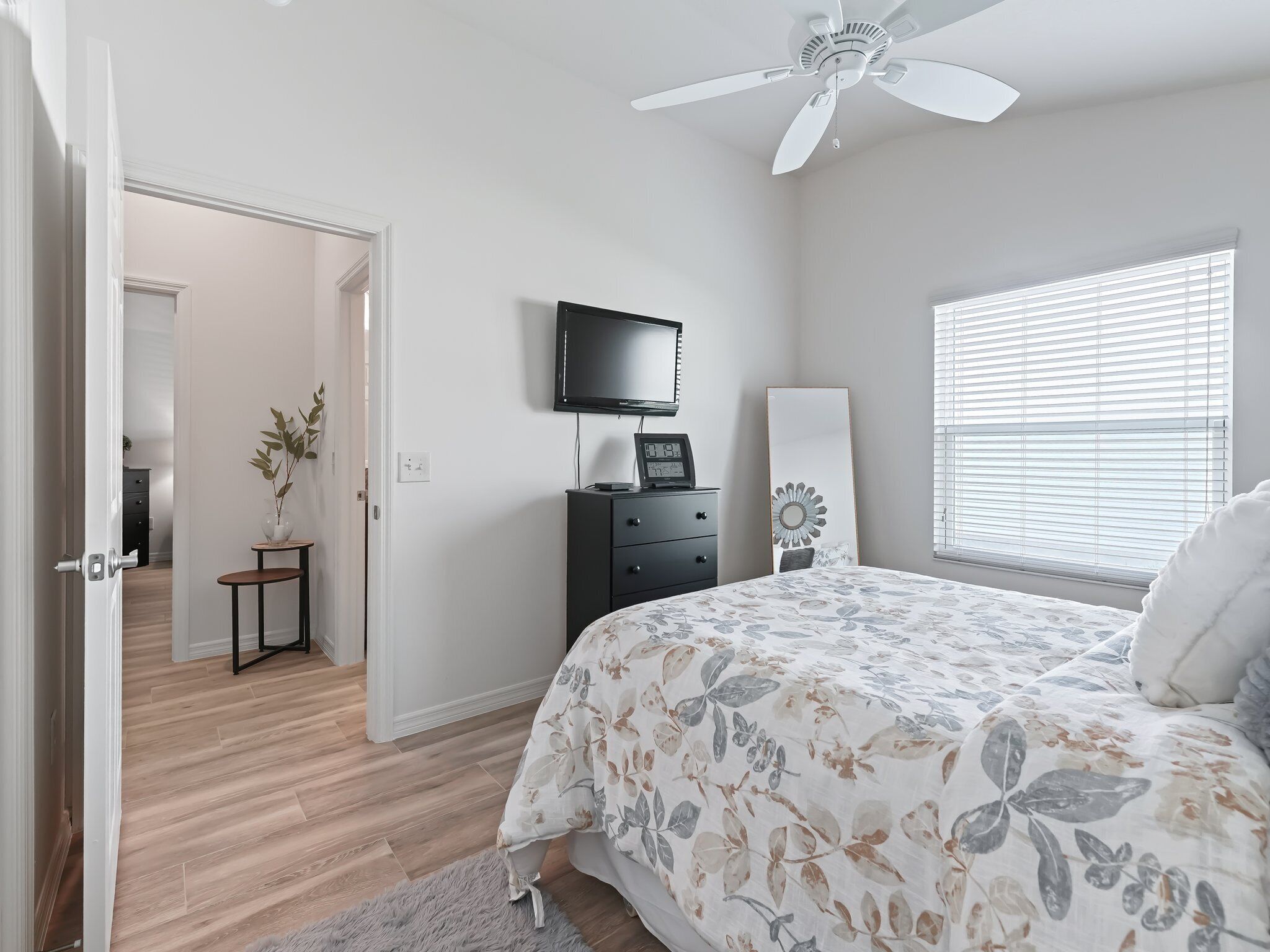 A bedroom with a bed, a ceiling fan, a TV, a dresser, and a window with blinds.