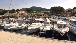 Un puerto deportivo con varias embarcaciones amarradas, rodeado de edificios y colinas al fondo.