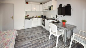 Una cocina compacta con armarios blancos, un microondas y un televisor de pantalla plana montado en la pared.