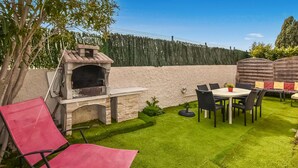 Un patio con una barbacoa de piedra, una mesa redonda con sillas y una sillona roja.