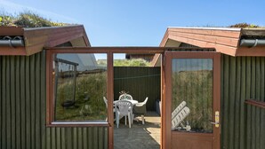 Una estructura de madera con un ventanal de vidrio que da a un patio con un columpio y una mesa con sillas.