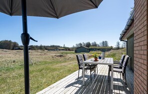 Enjoy a tranquil outdoor space with a table, chairs, and umbrella, overlooking a serene green building and lush surroundings.