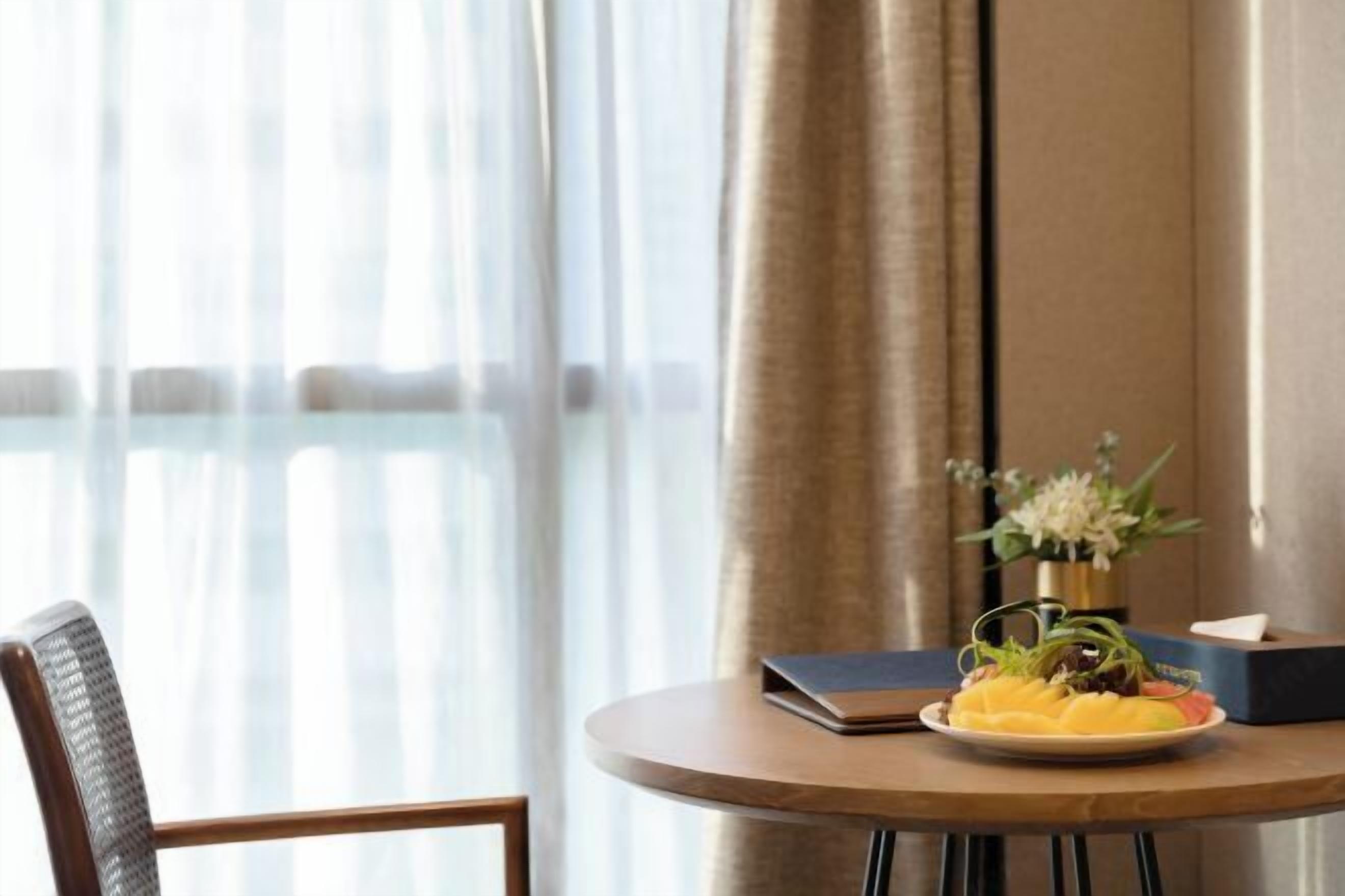 Una mesa redonda de madera con un ordenador portátil, un plato de fruta y un jarrón con flores.